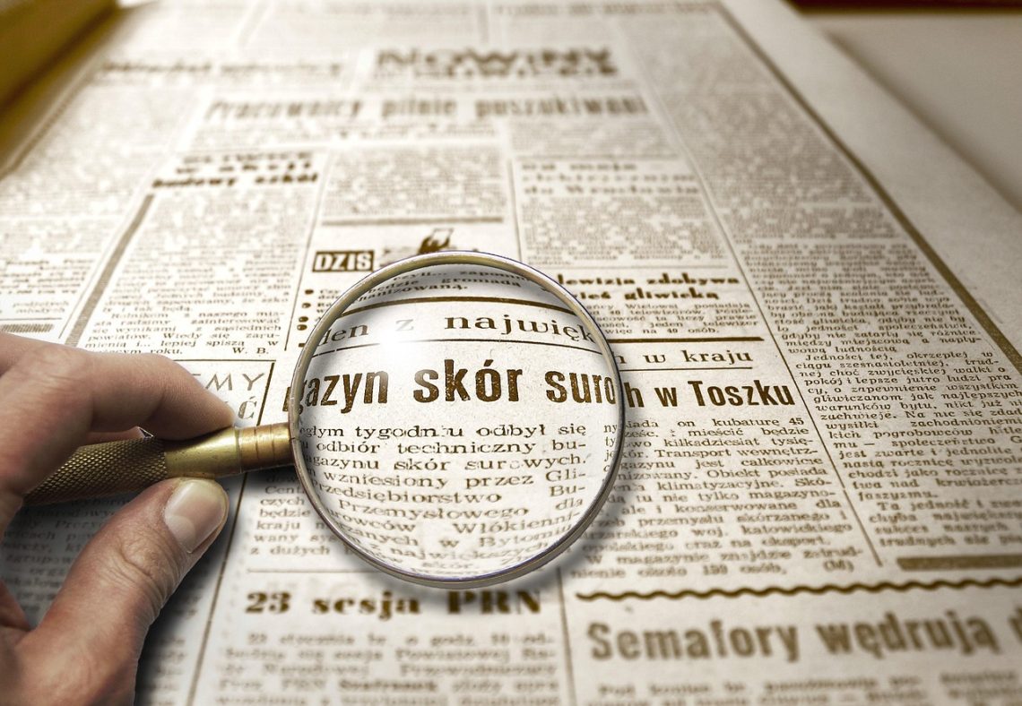 Lupa powiększająca tekst w starej gazecie, symbolizująca dokładne sprawdzanie informacji